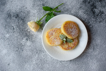 Tasty fresh cottage cheese pancakes on a white plate with a glass of milk on a concrete background. Healthy and diet breakfast