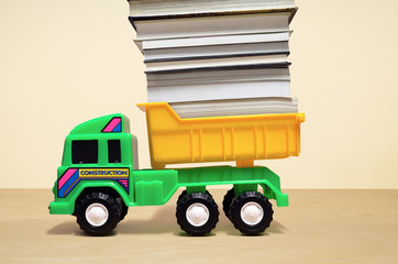 Pushing children too hard, illustrated by toy dump truck loaded with pile of books