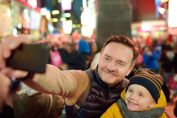 Little boy and his father taking selfie on Times Square in evening, downtown Manhattan.