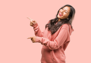 Portrait of fitness young indian woman pointing to the side, smiling surprised presenting something, natural and casual