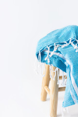 Blue and white striped cotton beach blanket with fringe folded on wooden stool on white wall...