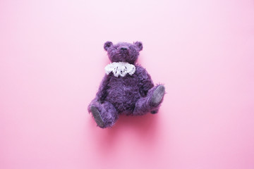 Purple furry vintage teddy bear with white lace jabot on the pastel pink background. Minimal...