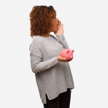 Young Black Woman Holding Piggy Bank Whispering Gossip Undertone