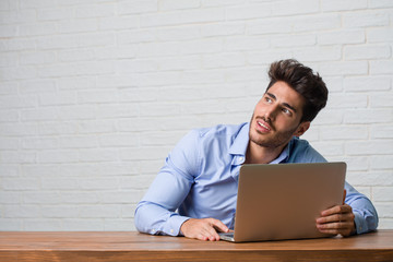 Young business man sitting and working on a laptop looking up, thinking of something fun and having an idea, concept of imagination, happy and excited