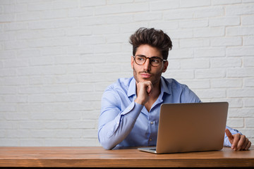 Young business man sitting and working on a laptop thinking and looking up, confused about an idea,...