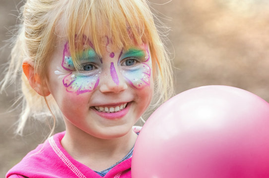 glückliches geschminktes Mädchen beim Kinderkarneval auf einem Freizeitpark mit einem Luftballon