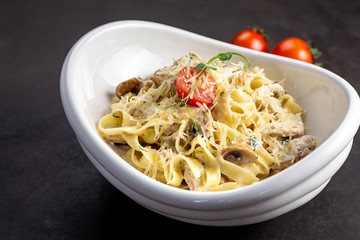 Pasta fettuccine with mushrooms and fried chicken ham in creamy cheese sauce. The black background is decorated with vegetables and a cutting board