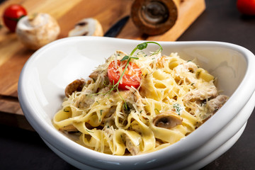 Pasta fettuccine with mushrooms and fried chicken ham in creamy cheese sauce. The black background is decorated with vegetables and a cutting board