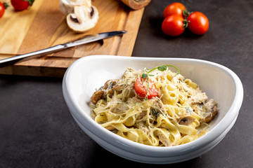 Pasta fettuccine with mushrooms and fried chicken ham in creamy cheese sauce. The black background is decorated with vegetables and a cutting board