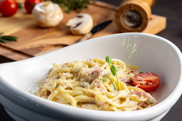 Pasta carbonara in a white plate with cherry tomatoes. Black background decorated with vegetables.