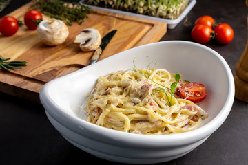 Pasta carbonara in a white plate with cherry tomatoes. Black background decorated with vegetables.