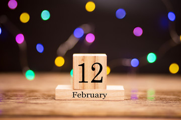 February 12th. Day 12 of february month set on wooden calendar at center of dark background with garland bokeh. Winter time. Empty space for text, mockup. Darwin Day. Day of Marriage Agencies