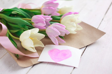 women's Day. a bouquet of tulips on a white wooden background with a card with hearts. selective focus