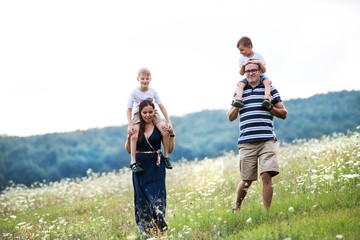 A father and mother giving piggyback ride to small sons in nature on a summer day.