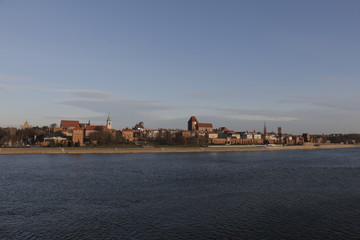 Fototapeta premium View of Torun from the bridge. In the foreground the river. In the background, the Vistula embankment, medieval defensive walls, the Old Town, the New Town, the Teutonic Castle, historic buildings.
