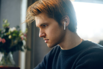 Man in wireless headphones at resaurant, street, restaurant. Man listening to e-book, the guy is listening to music. A man in bluetooth headphones is enjoying life look at the laptop. Fashion