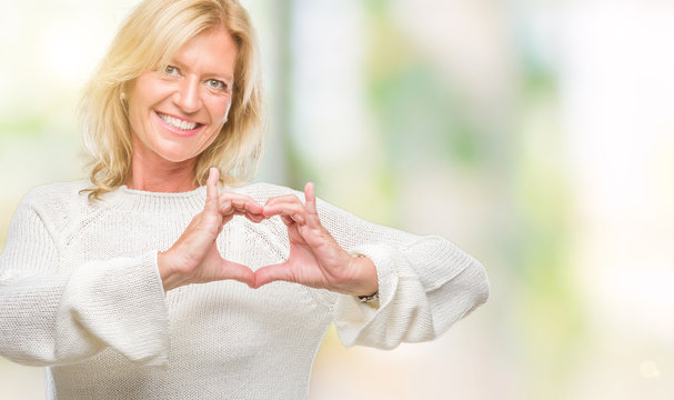 Middle age blonde woman wearing winter sweater isolated background smiling in love showing heart symbol and shape with hands. Romantic concept.