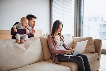 Obraz premium A portrait of young couple with a baby and laptop at home.