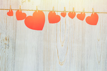 Red and pink hearts are cut out of paper, suspended from rope with clothespins. Valentine's Day celebration concept