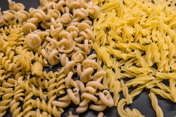 Variety of types and shapes of dry Italian pasta. Set of raw dry pasta on a black slate background.