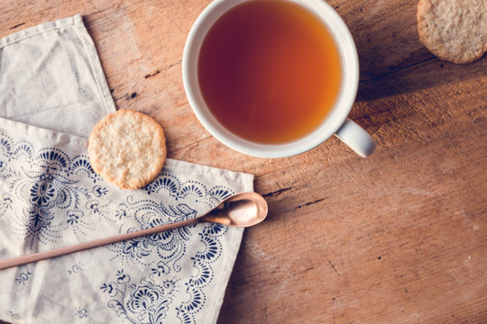 Tee in weißer Tasse auf Holztisch mit Geschirrtuch und kupferfarbenen Löffel