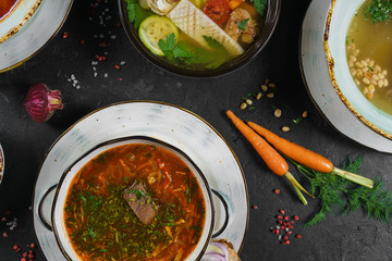 soup, with raw beef, bone broth in a stainless pan, soy sprouts, spices, baked onion, rice noodle, fresh coriander and mint on black wooden table, view from above. soup and soup on the table