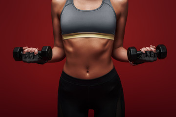 Love yourself enough to work harder. Sportswoman holds dumbbells standing over red background