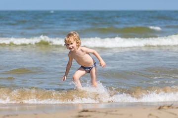 Fototapeta premium Young caucasian boy playing on sea shore at sunny summer