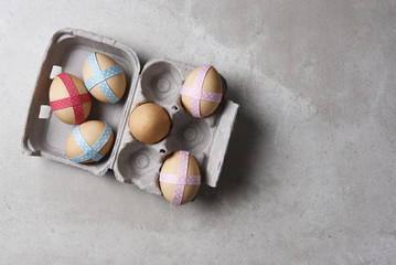 Ribbon decorated brown eggs in a carton on gray tile surface.