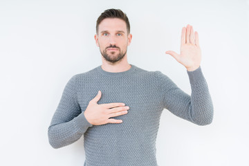 Young handsome man wearing casual sweater over isolated background Swearing with hand on chest and...