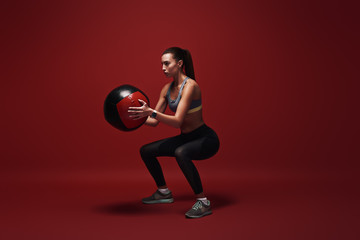 Awesome exercise. Sportswoman holds exercise ball standing over red background