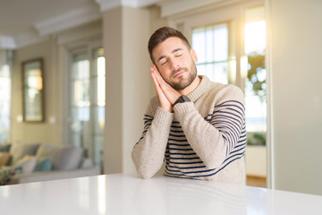 Fototapeta premium Young handsome man at home sleeping tired dreaming and posing with hands together while smiling with closed eyes.