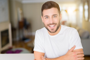 Young handsome man wearing casual white t-shirt at home happy face smiling with crossed arms looking at the camera. Positive person.
