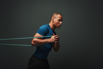 Pushing hard. Sportsman working out with resistance band over dark background - obrazy, fototapety, plakaty