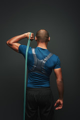 Give your best. Sportsman standing with resistance band over dark background. Back view