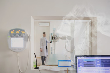 the picture of a male radiologist adjusting the X-ray machine behind the screen