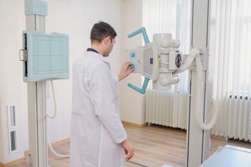  back view of a male radiologist adjusting the X-ray machine in examination rom