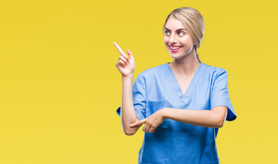Young beautiful blonde doctor surgeon nurse woman over isolated background with a big smile on face, pointing with hand and finger to the side looking at the camera.