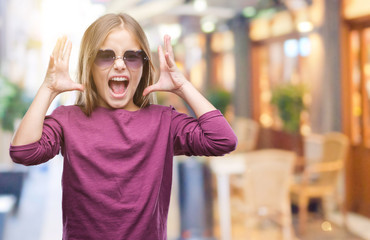 Fototapeta premium Young beautiful girl wearing sunglasses over isolated background celebrating mad and crazy for success with arms raised and closed eyes screaming excited. Winner concept