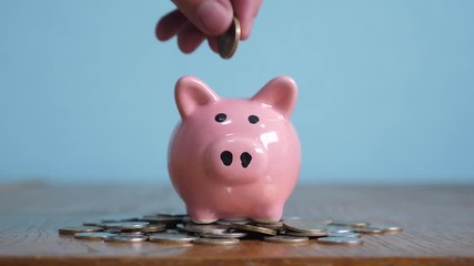piggy bank business standing on a pile of coins concept. A hand is putting coin in a piggy bank on a yellow background. saving money is an investment for the future. Banking investment and lifestyle - Powered by Adobe