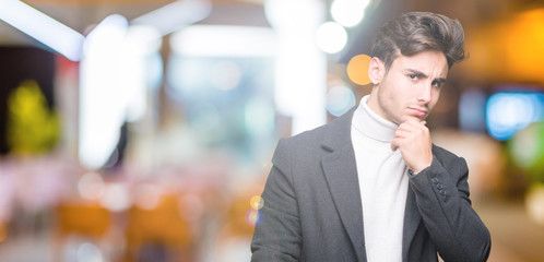 Young elegant man wearing winter coat over isolated background with hand on chin thinking about question, pensive expression. Smiling with thoughtful face. Doubt concept.