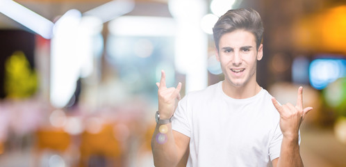 Young handsome man wearing white t-shirt over isolated background shouting with crazy expression doing rock symbol with hands up. Music star. Heavy concept.