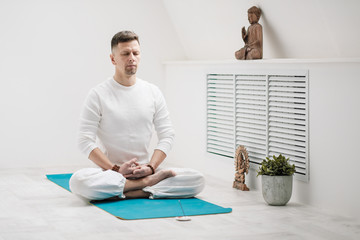 Male brunette with a beard in white clothes on a white background with his hands folded on his chest. Meditation and prayer, yoga.