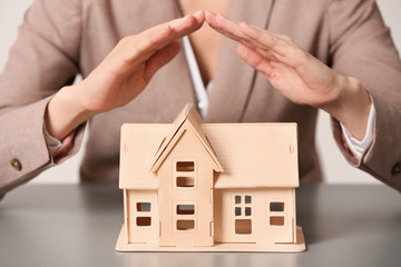 Female agent covering house model at table, closeup. Home insurance