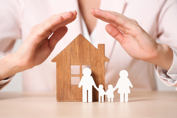 Female agent covering wooden house and family at table, closeup. Home insurance