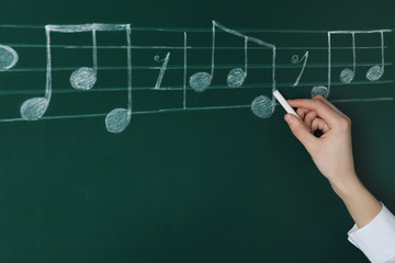 Woman writing music notes with chalk on blackboard, closeup