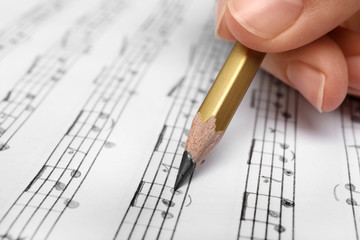 Woman writing music notes on sheet with pencil, closeup