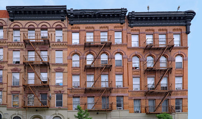 old brown brick New York apartment building with external fire escape ladders - obrazy, fototapety, plakaty