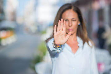 Beautiful middle age hispanic woman at the city street on a sunny day with open hand doing stop sign with serious and confident expression, defense gesture