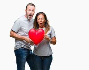 Fototapeta na wymiar Middle age hispanic casual couple in love holding red heart over isolated background scared in shock with a surprise face, afraid and excited with fear expression